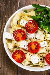 Pasta with tomatoes and white cheese on wooden table