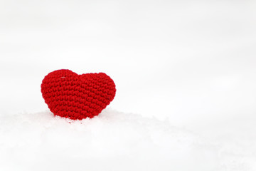 Red knitted heart on the snow, symbol of love with snowflakes. Background for Christmas holiday, Valentine's day greeting card, concept of romantic celebration