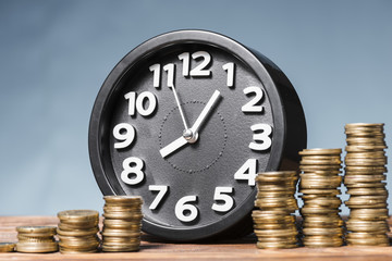Round alarm clock with stack of increasing coins against blue background