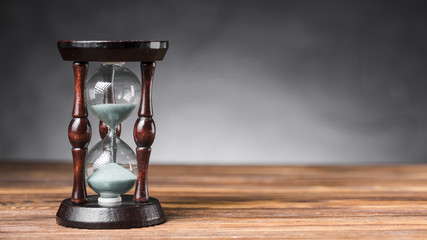 Transparent sand hourglass on wooden desk against gray background © Freepik