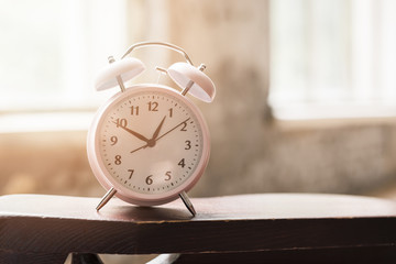 Naklejka premium Pink alarm clock on wooden table in sunlight