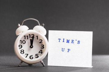 Times up blue text on adhesive note near the white alarm clock against black backdrop