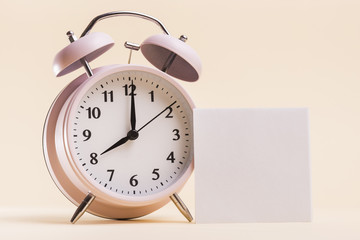Pink alarm clock with blank white adhesive note on beige background
