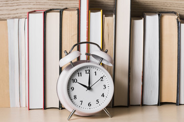 White alarm clock showing 10'o clock in front of bookshelf on wooden desk