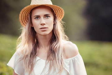Portrait of beautiful charming young blonde girl in romantic dress and hat posing on nature on...
