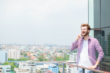 Fototapeta na wymiar Handsome casual businessman talking with smartphone on top of building.