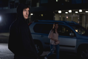 selective focus of thief looking at camera near woman walking at nighttime