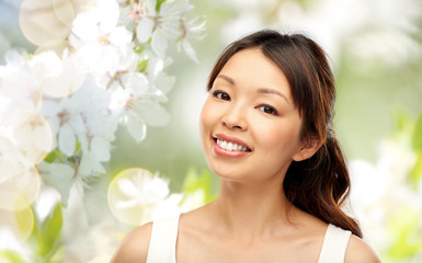 beauty and people concept - face of happy smiling young asian woman over natural spring cherry blossom background