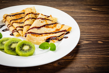 Crepes with kiwi and cream on wooden background