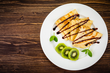 Crepes with kiwi and cream on wooden background
