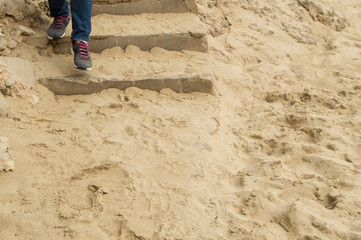 Legs in jeans and sneakers descending a stone staircase covered with sand, the concept of tourism,...