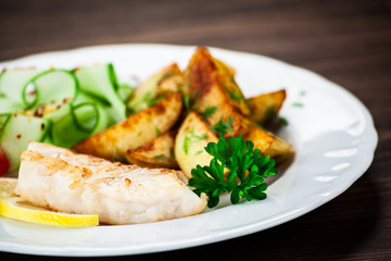 Fried fish with baked potatoes on wooden table
