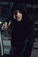 aggressive thief in black hoodie pointing gun at car window