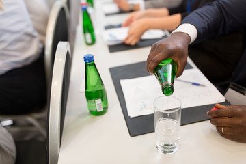 business and people concept - close up of african american businessman pouring water from bottle to glass at conference