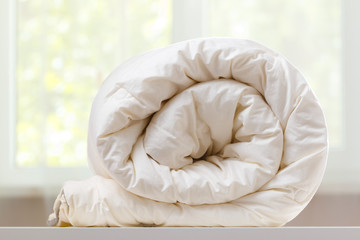 A folded rolls duvet is lying on the dresser against the background of a blurred window. Household.