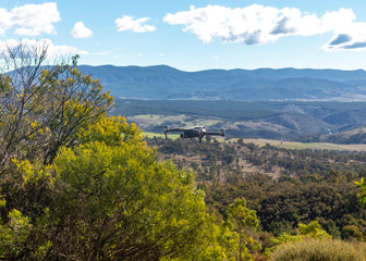 Fototapeta premium A small modern unmanned aerial vehicle drone in flight showing telegraph wires, landscape views and country scenery looking west of Canberra in the Australian Capital Territory