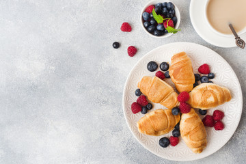 Croissants with fresh raspberries and blueberries on a dark concrete background. Copy space. concept of Breakfast coffee honey.