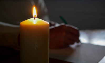 Caucasian man writing a letter  on pine wood table, shallow depth of field, focu on the candle light.