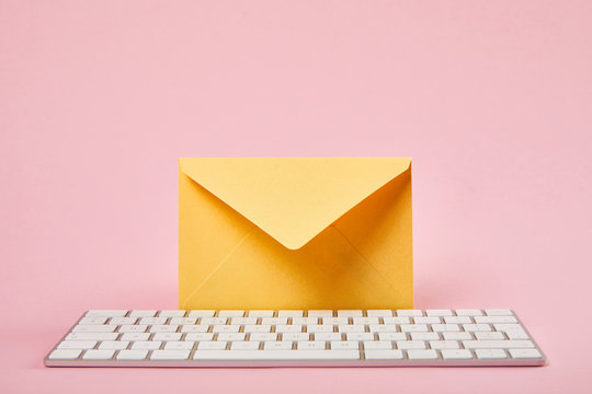 yellow envelope near white computer keyboard on pink background