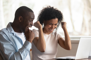 Overjoyed african couple celebrate online victory sit at table