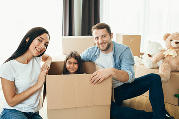 Happy couple unpacking boxes and having fun with daughter in living room at new home