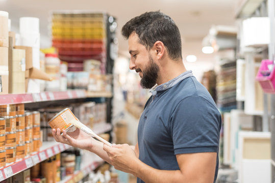 Bearded man in craft store selecting paint for work at home