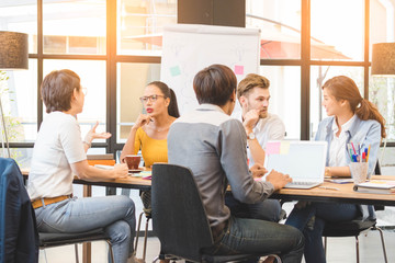 Group of five casual business meeting to discuss ideas and laptop on table in office.