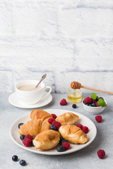 Croissants with fresh raspberries and blueberries on a dark concrete background. Copy space. concept of Breakfast coffee honey.