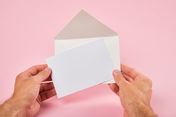 cropped view of man holding envelope and blank white card on pink background