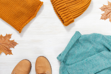 Autumn female outfit. Set of clothes and shoes on white background. Warm green knitted sweater, cap and snood orange colored, leather shoes. View from above. Copy space.
