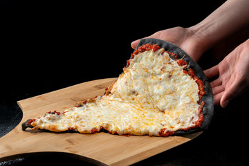 A slice of pizza from black dough lying on a wooden board.