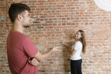 Young couple doing apartment repair together themselves. Married man and woman doing home makeover or renovation. Concept of relations, family, love. Discuss painting the wall or preparing it for.