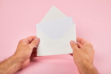 cropped view of man holding envelope with blank white card on pink background