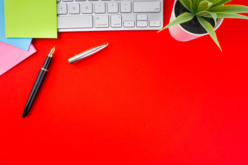 Flat lay, top view office table desk. Workspace with pen, decoration vase, sticky notes and keyboard on the red background. Business Finance, Education, Technology and Copy Space concept