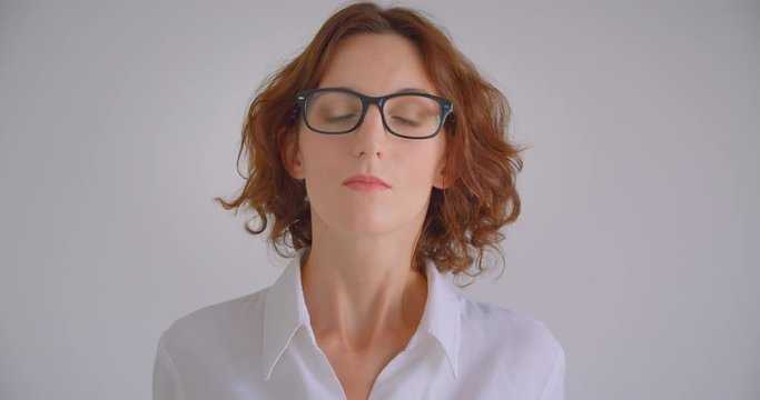 Closeup portrait of adult redhead caucasian businesswoman in glasses looking at camera indoors in the white apartment