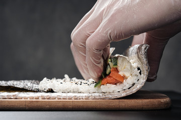 Cook's hands close-up. A male chef makes sushi and rolls from rice, red fish and avocado. White...