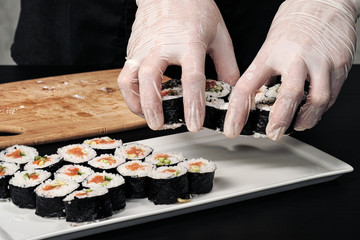 Cook's hands close-up. A male chef makes sushi and rolls from rice, red fish and avocado. White gloves.