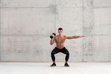 Muscular shirtless caucasian male athlete performs a dumbbell weightlifting exercise in a grungy concrete structure while showing his six pack abs 