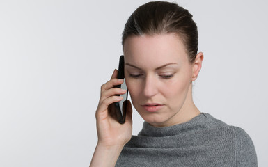 Young woman in grey sweater is listening at a cell phone