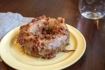 Maple Bacon iced donut on a yellow plate for breakfast