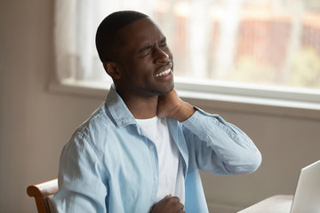 African man frowning massaging pinched nerve feels pain in neck