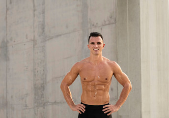 Shirtless caucasian muscular athlete standing against a concrete wall  sweating as he rest during exercise showing his six pack abs  