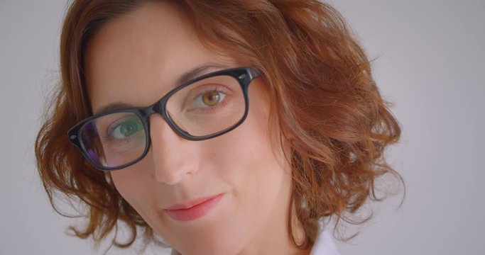 Closeup macro portrait of adult redhead caucasian businesswoman in glasses looking at camera indoors in the white apartment