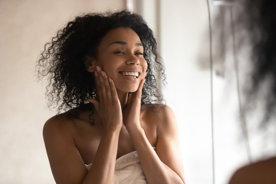 African woman after shower look in mirror touching gentle skin