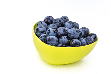 Ripe plums in the yellow bowl with white background. The summer harvest.
