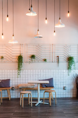 Coffee house interior with wooden table and chairs decorated with hanging bush. Minimal style decoraion.