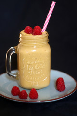 Mango and banana smoothie decorated with raspberries and reusable straw. Selective focus.