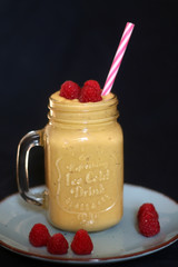 Mango and banana smoothie decorated with raspberries and reusable straw. Selective focus.