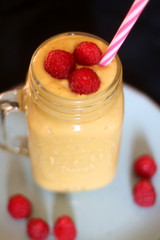 Mango and banana smoothie decorated with raspberries and reusable straw. Selective focus.