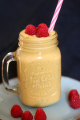 Mango and banana smoothie decorated with raspberries and reusable straw. Selective focus.